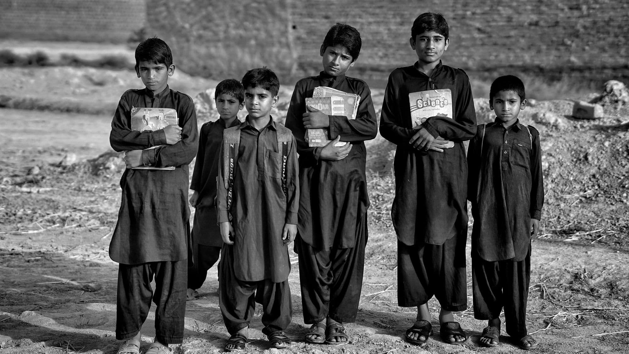 A black and white photograph of six boys standing outdoors holding schoolbooks