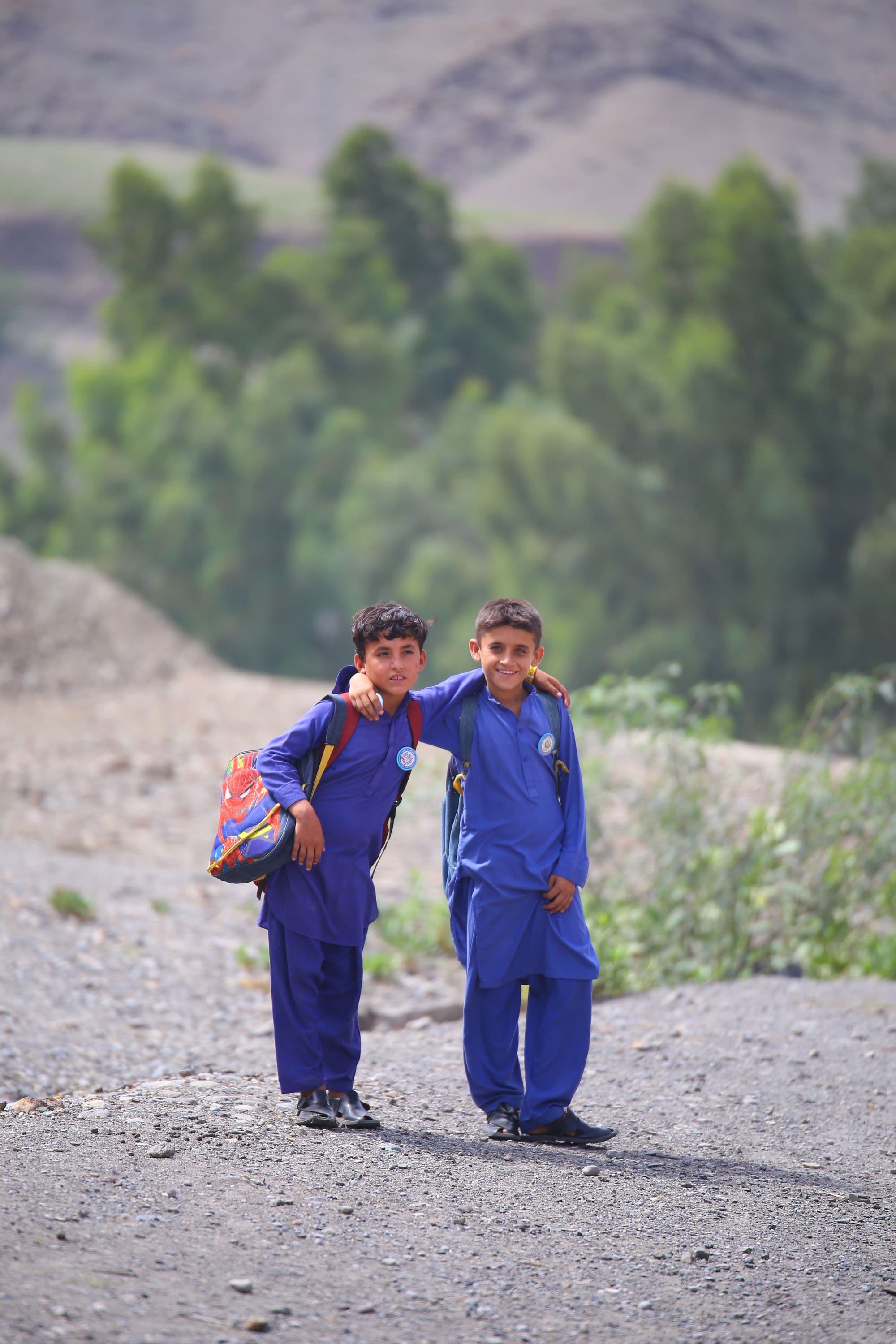 Two schoolboys in blue uniforms walking together with their backpacks, one with an arm around the other