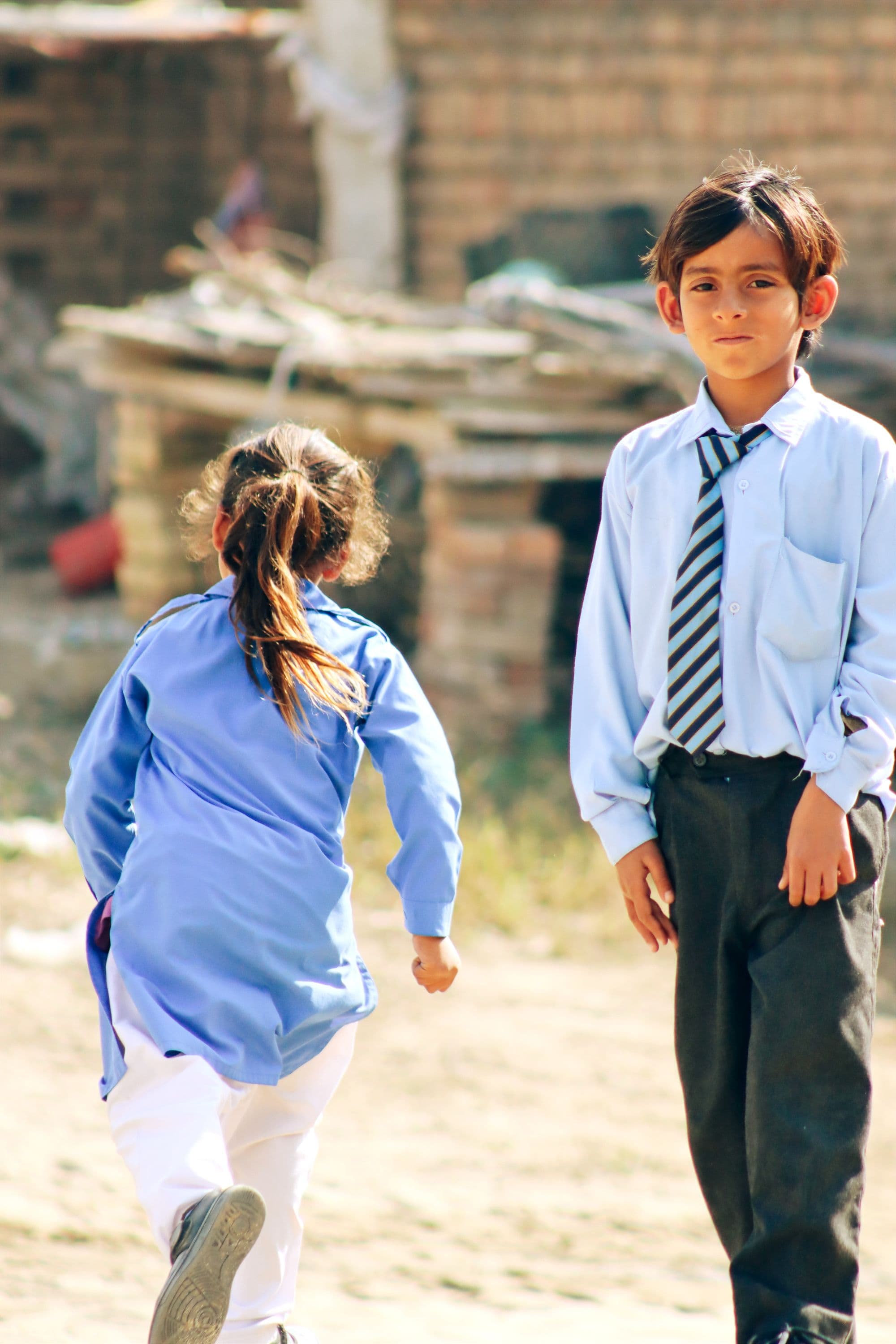 Two children in school uniform in a schoolyard, one running