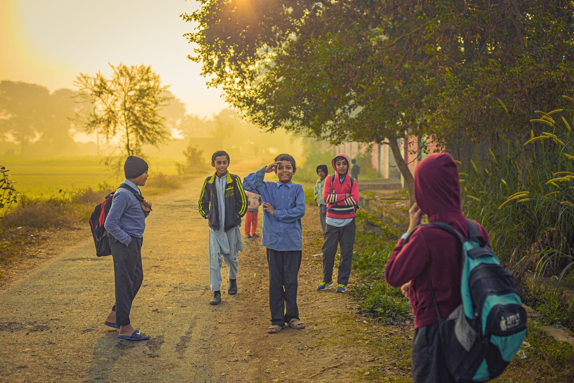 Children with backpacks walking along a rural path at sunrise on their way to school